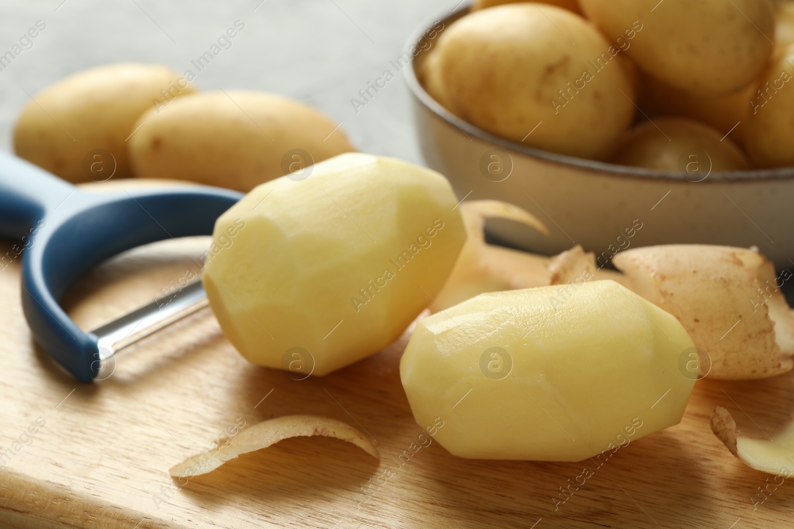 Photo of Fresh raw potatoes and peeler on table, closeup