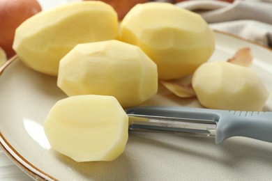 Photo of Fresh raw potatoes and peeler on table, closeup