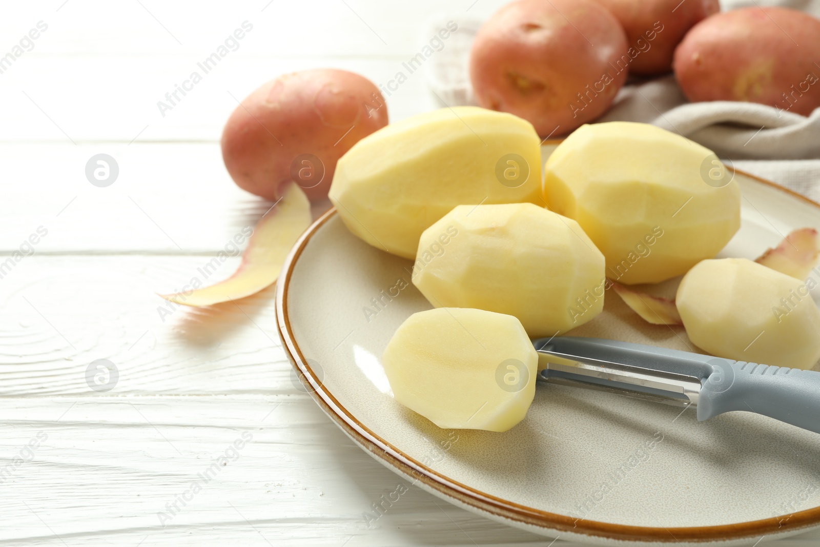 Photo of Fresh raw potatoes and peeler on white wooden table, closeup. Space for text