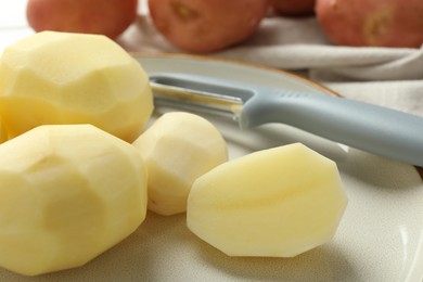 Photo of Fresh raw potatoes and peeler on table, closeup