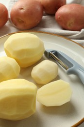 Photo of Fresh raw potatoes and peeler on table, closeup