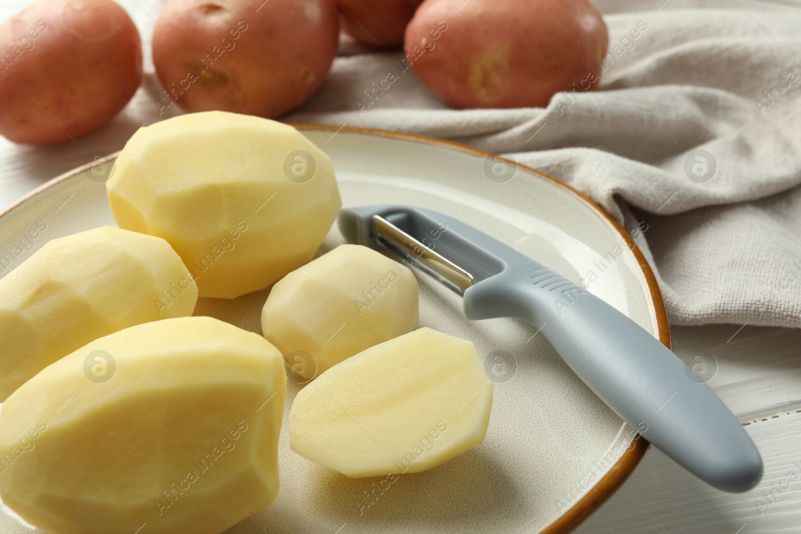 Photo of Fresh raw potatoes and peeler on table, closeup