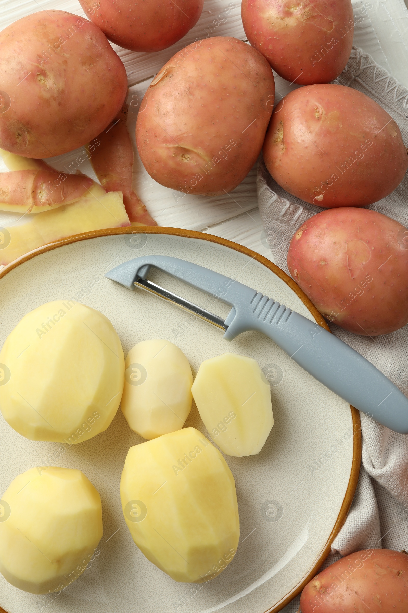 Photo of Fresh raw potatoes and peeler on white wooden table, flat lay