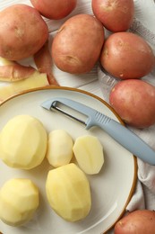 Photo of Fresh raw potatoes and peeler on white wooden table, flat lay