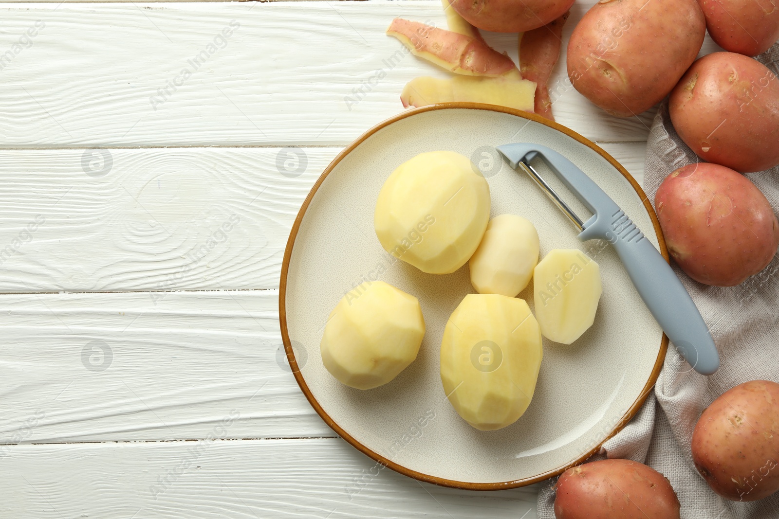 Photo of Fresh raw potatoes and peeler on white wooden table, flat lay. Space for text