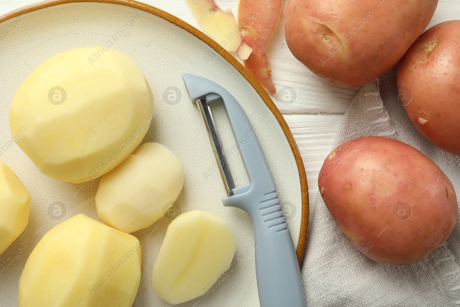 Photo of Fresh raw potatoes and peeler on white wooden table, flat lay