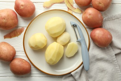 Fresh raw potatoes and peeler on white wooden table, flat lay