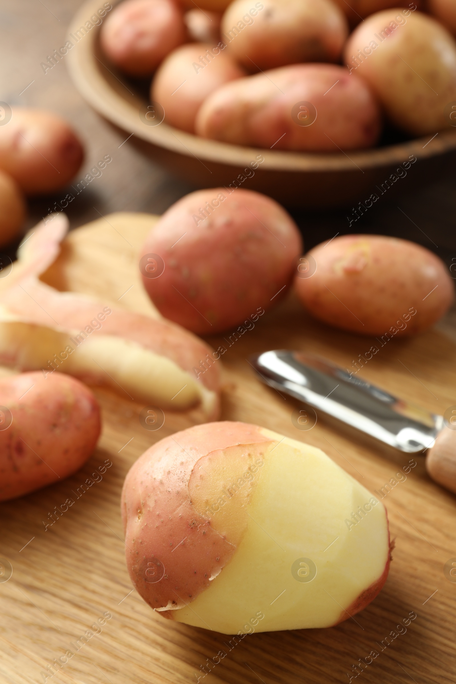 Photo of Fresh raw potatoes, peels and peeler on wooden table