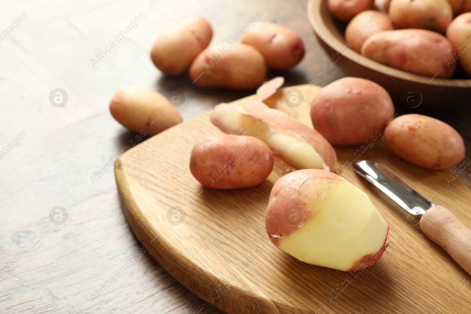 Photo of Fresh raw potatoes, peels and peeler on wooden table