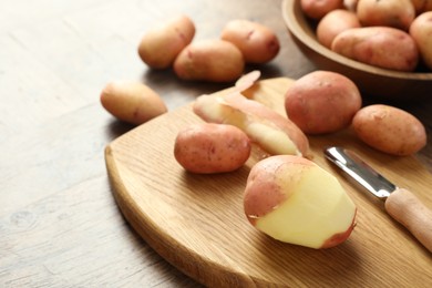 Fresh raw potatoes, peels and peeler on wooden table