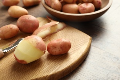 Photo of Fresh raw potatoes, peels and peeler on wooden table