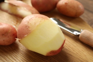 Photo of Fresh raw potatoes, peels and peeler on wooden table, closeup