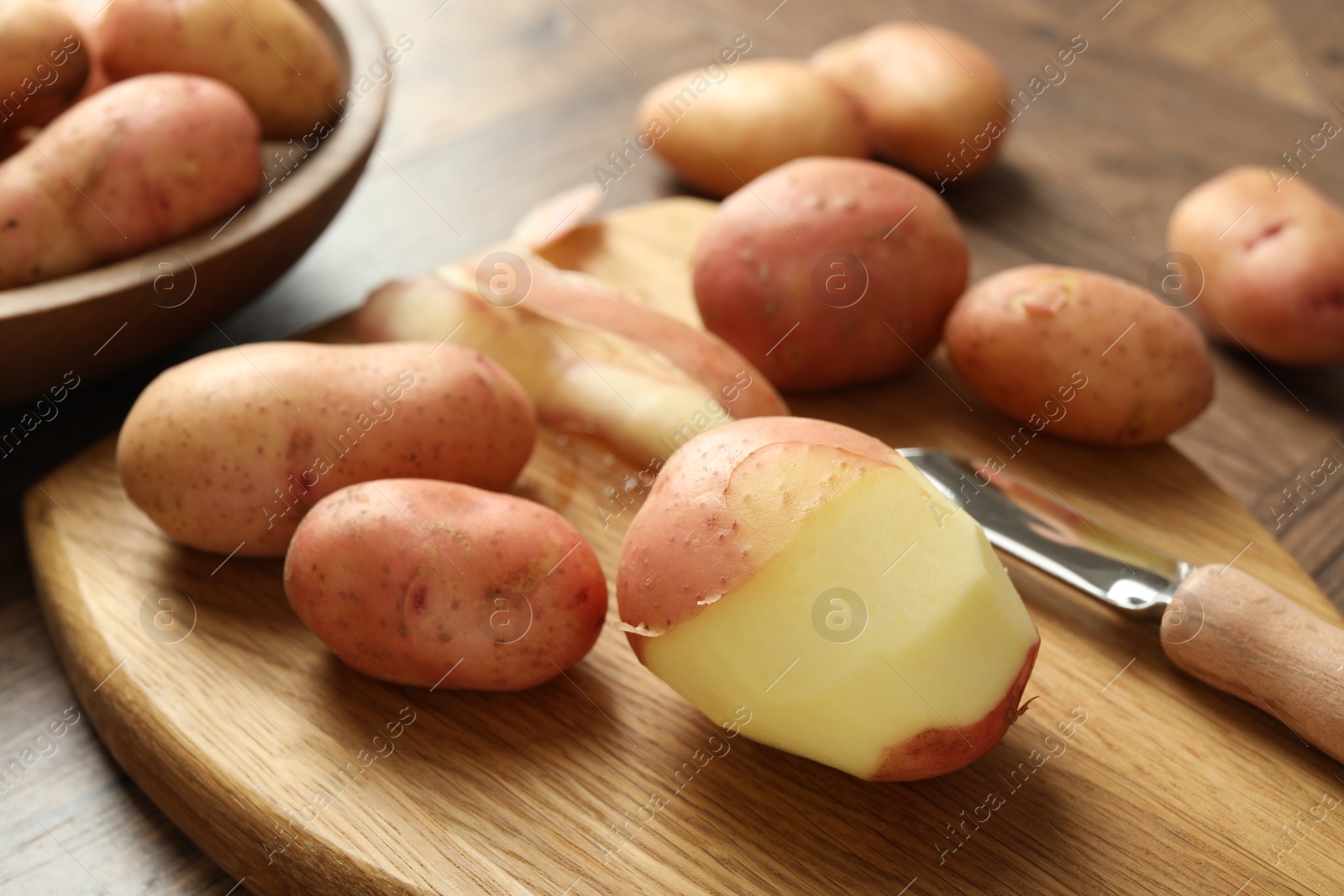 Photo of Fresh raw potatoes, peels and peeler on wooden table, closeup