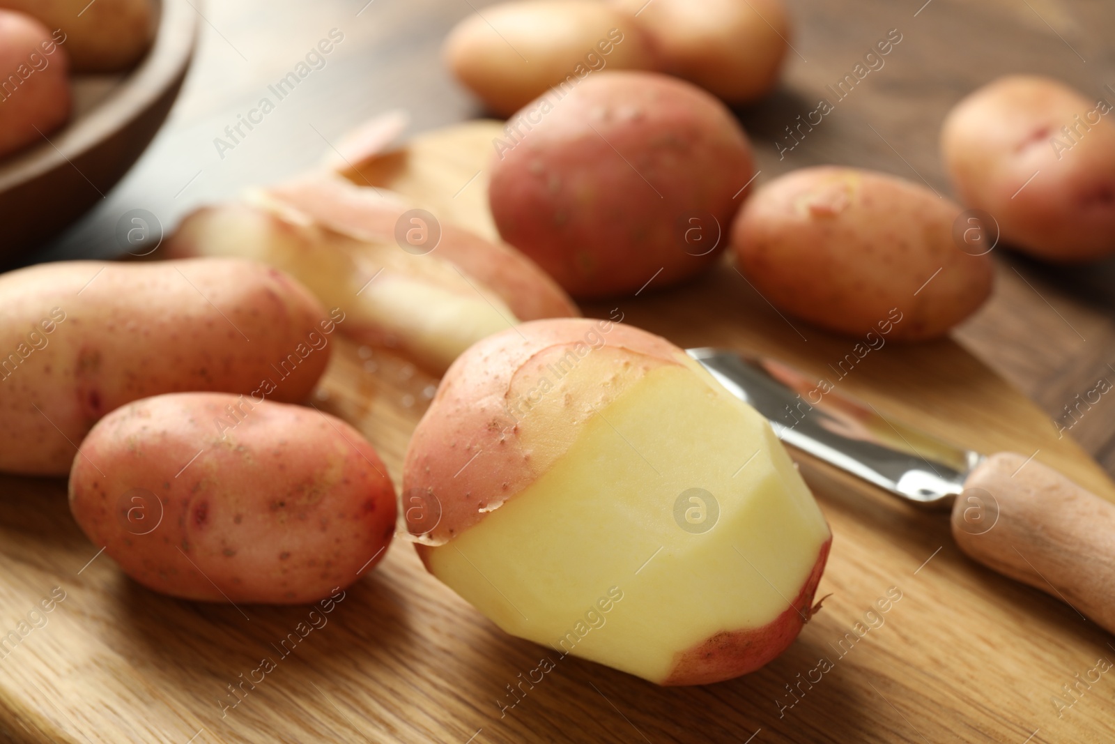 Photo of Fresh raw potatoes, peels and peeler on wooden table, closeup