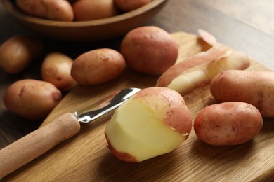 Photo of Fresh raw potatoes, peels and peeler on wooden table