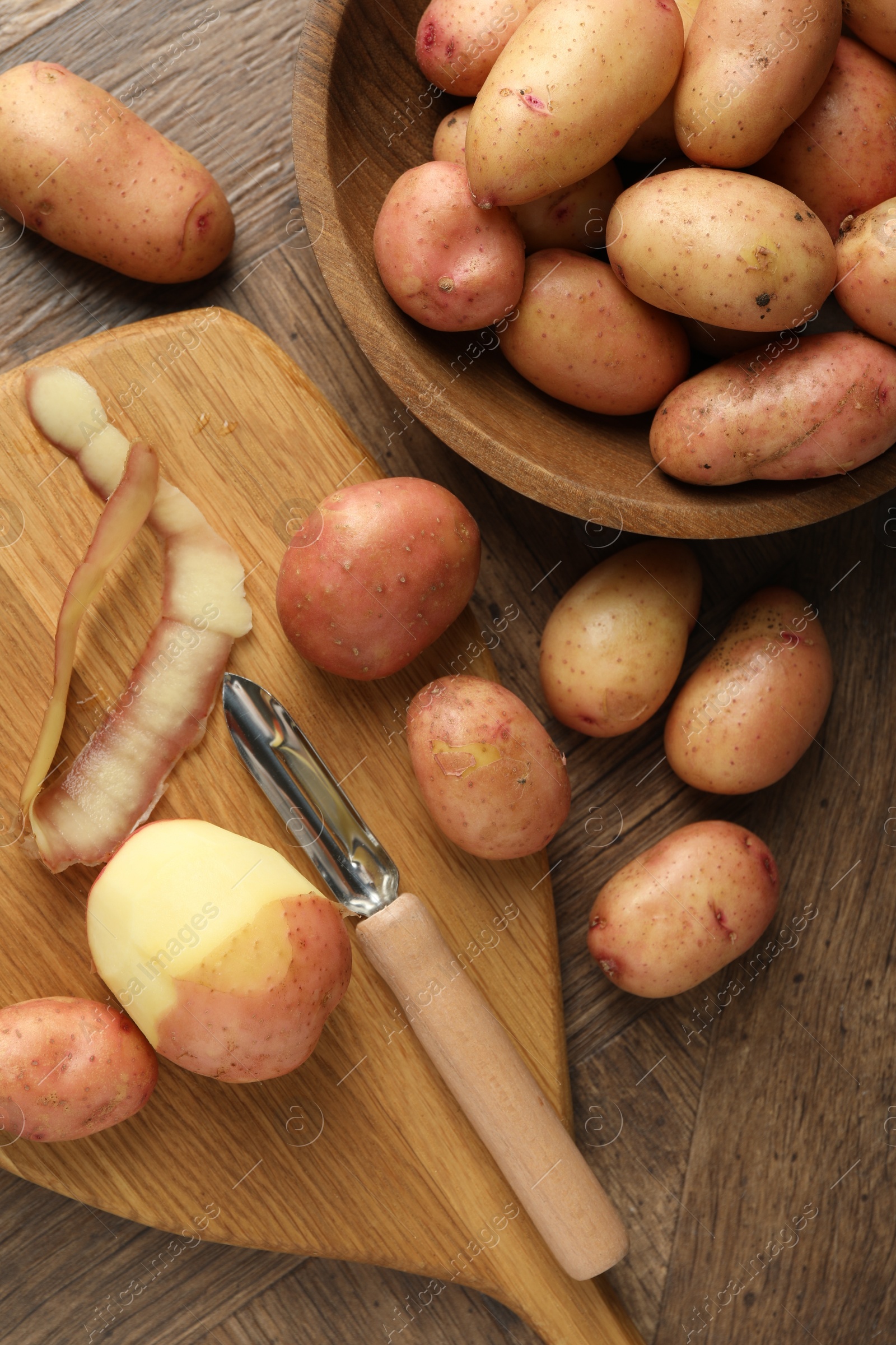 Photo of Fresh raw potatoes, peels and peeler on wooden table, flat lay