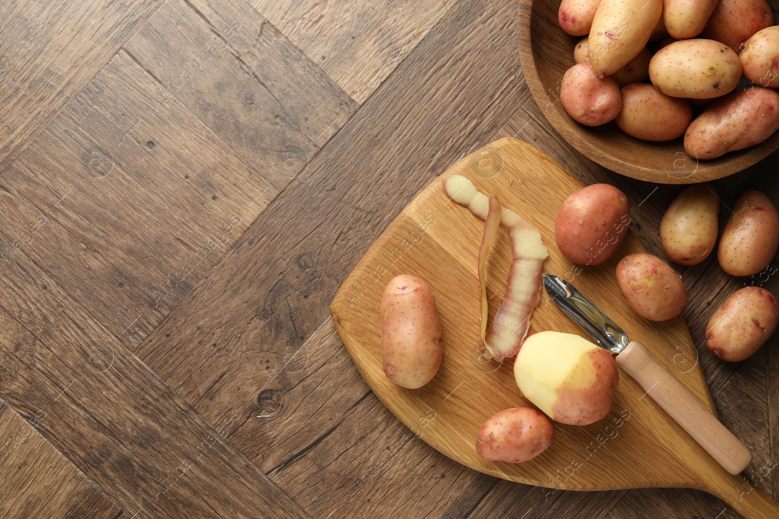 Photo of Fresh raw potatoes, peels and peeler on wooden table, flat lay. Space for text