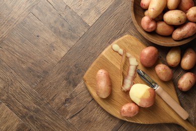 Fresh raw potatoes, peels and peeler on wooden table, flat lay. Space for text