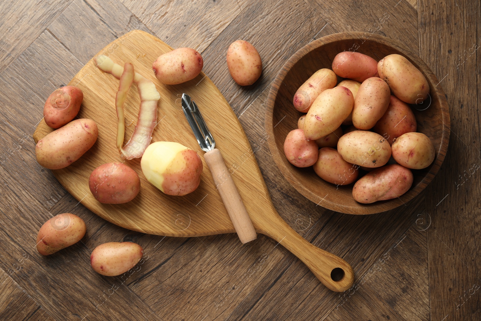 Photo of Fresh raw potatoes, peels and peeler on wooden table, flat lay