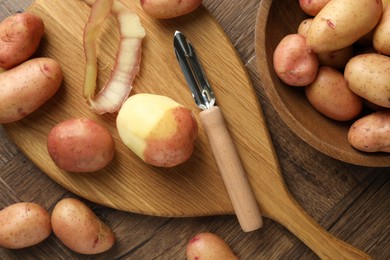 Fresh raw potatoes, peels and peeler on wooden table, flat lay