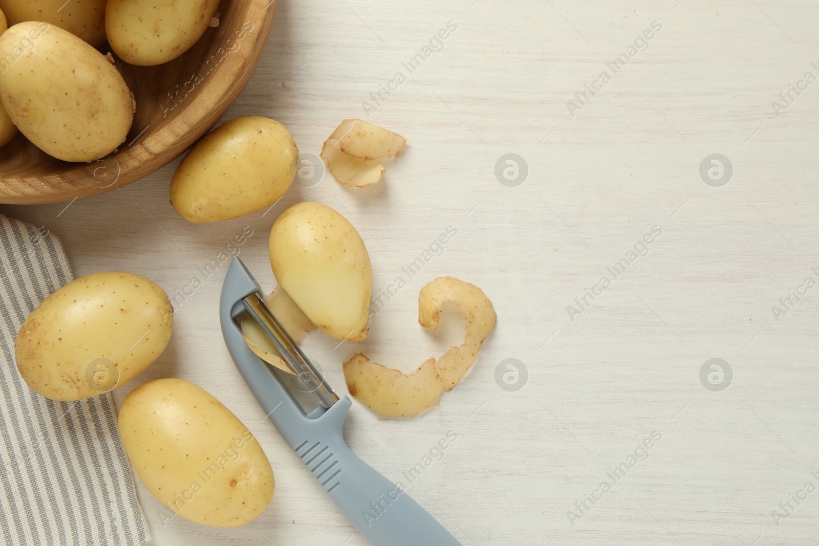 Photo of Fresh raw potatoes, peels and peeler on white wooden table, flat lay. Space for text