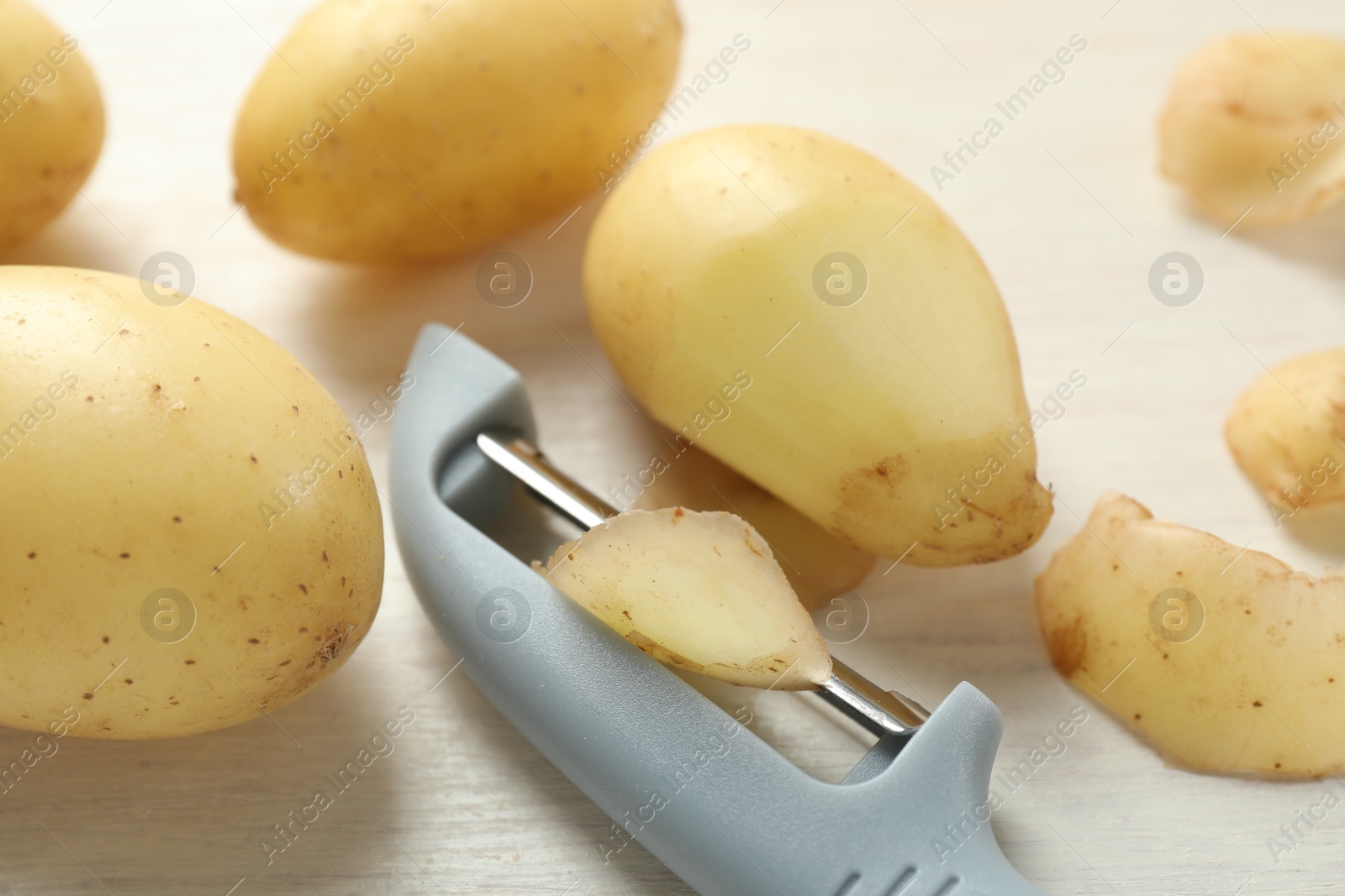 Photo of Fresh raw potatoes, peels and peeler on white wooden table, closeup