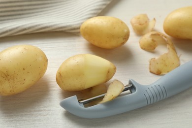 Photo of Fresh raw potatoes, peels and peeler on white wooden table