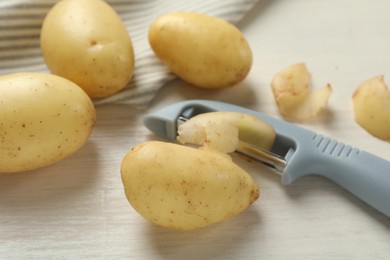 Fresh raw potatoes, peels and peeler on white wooden table