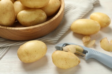 Photo of Fresh raw potatoes, peels and peeler on white wooden table