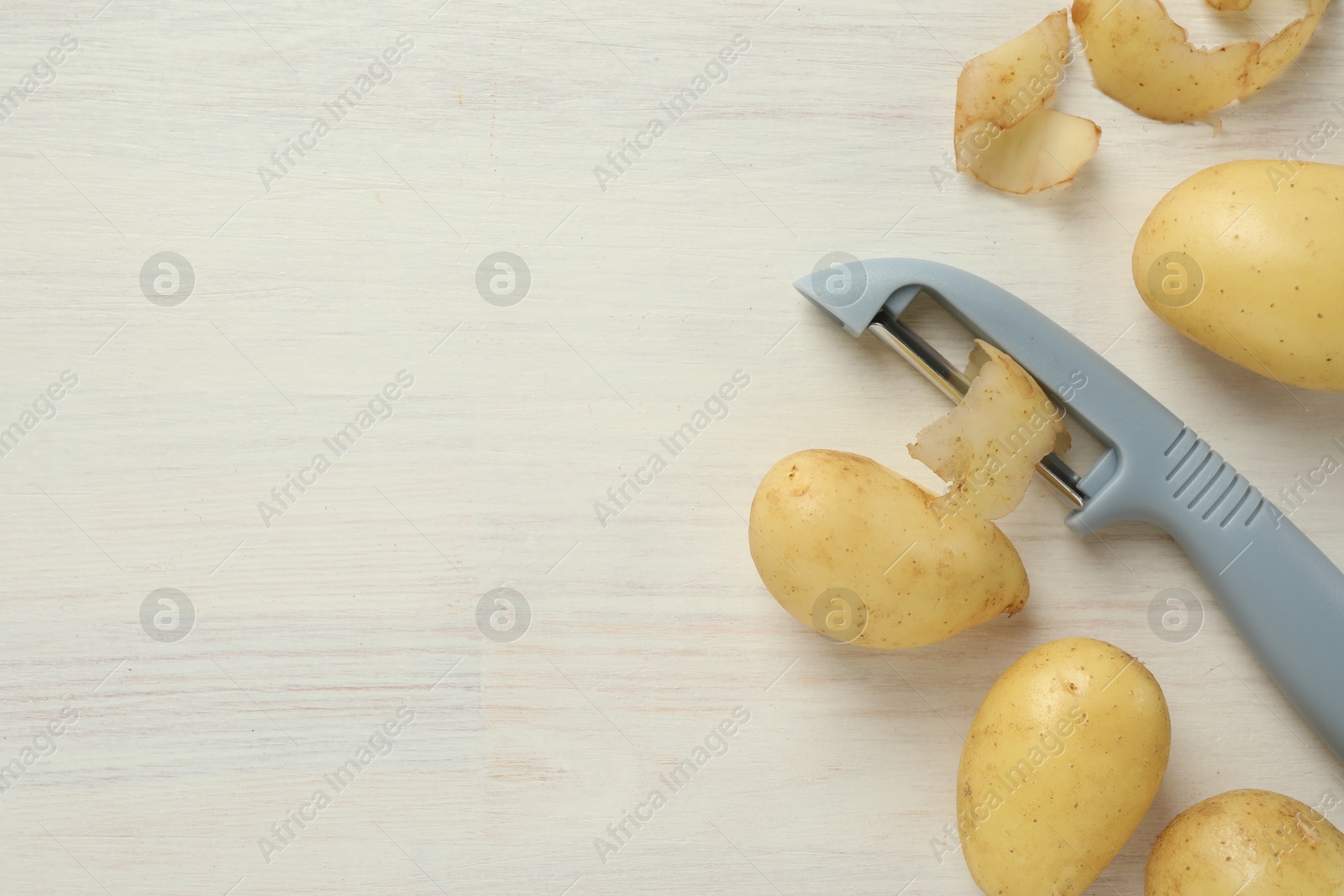 Photo of Fresh raw potatoes, peels and peeler on white wooden table, flat lay. Space for text