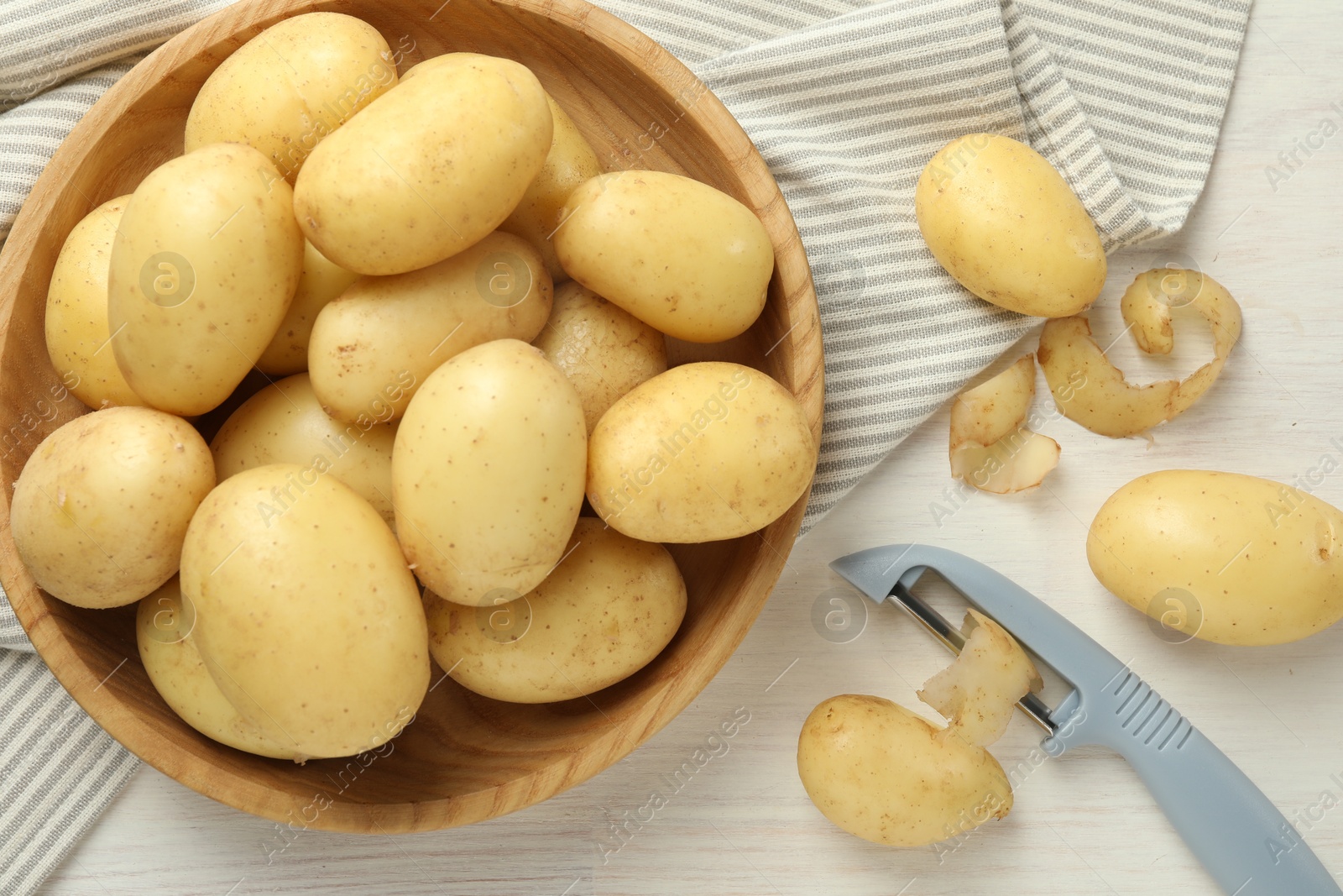 Photo of Fresh raw potatoes, peels and peeler on white wooden table, flat lay