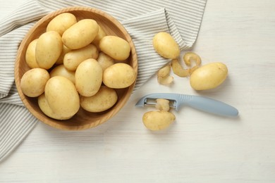 Photo of Fresh raw potatoes, peels and peeler on white wooden table, flat lay