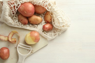 Fresh raw potatoes, peels and peeler on white wooden table, flat lay. Space for text