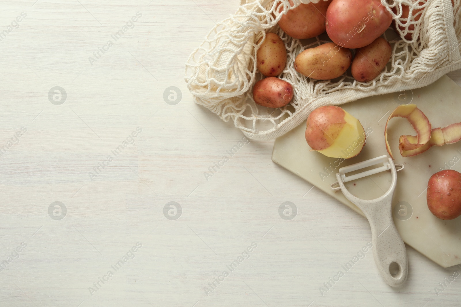 Photo of Fresh raw potatoes, peels and peeler on white wooden table, flat lay. Space for text