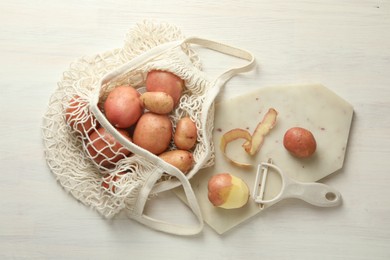 Photo of Fresh raw potatoes, peels and peeler on white wooden table, flat lay