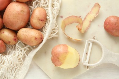 Photo of Fresh raw potatoes, peels and peeler on white wooden table, flat lay