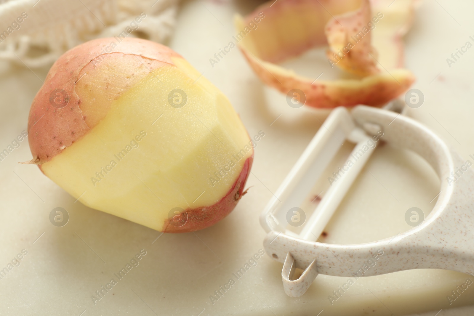 Photo of Fresh raw potatoes, peels and peeler on white wooden table, closeup