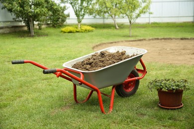 Wheelbarrow with soil on green grass outdoors