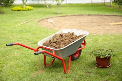 Wheelbarrow with soil on green grass outdoors