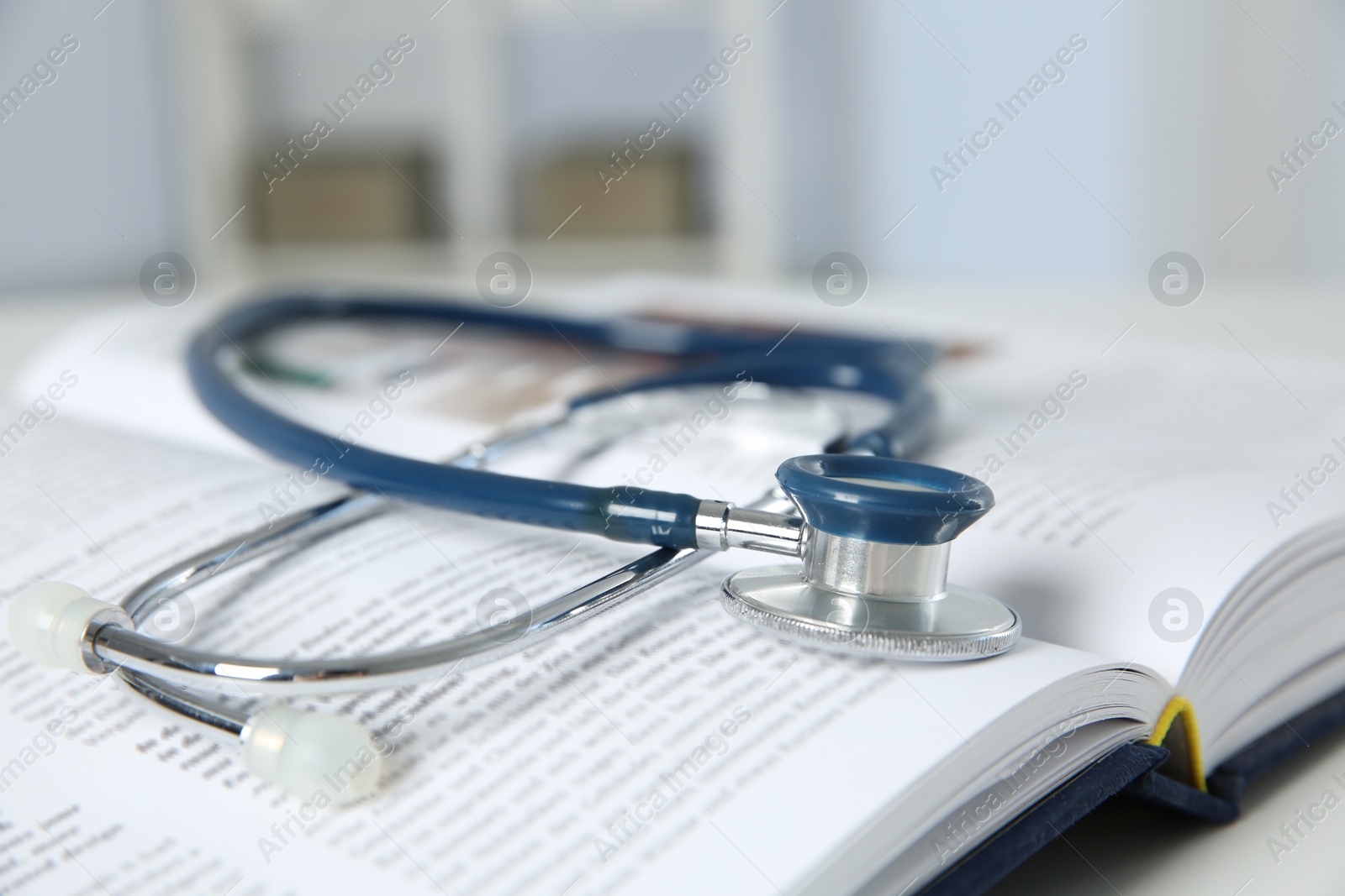 Photo of One medical stethoscope and book on white table, closeup