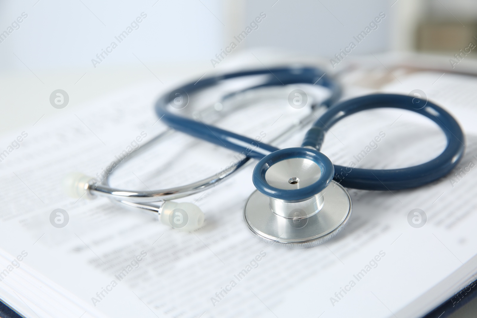 Photo of One medical stethoscope and book on table, closeup