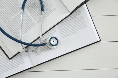 Photo of One new medical stethoscope and books on white wooden table, top view