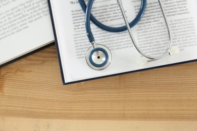 One new medical stethoscope and books on wooden table, top view. Space for text