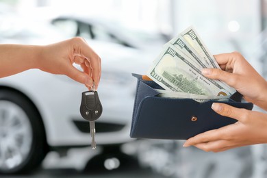 Image of Woman giving money to seller in exchange for car key in shop, closeup. Buying auto