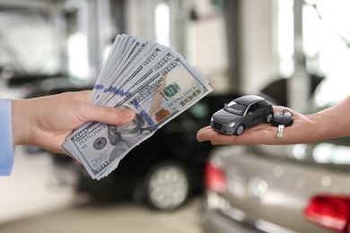 Image of Woman giving money to seller in exchange for car key in shop, closeup. Buying auto