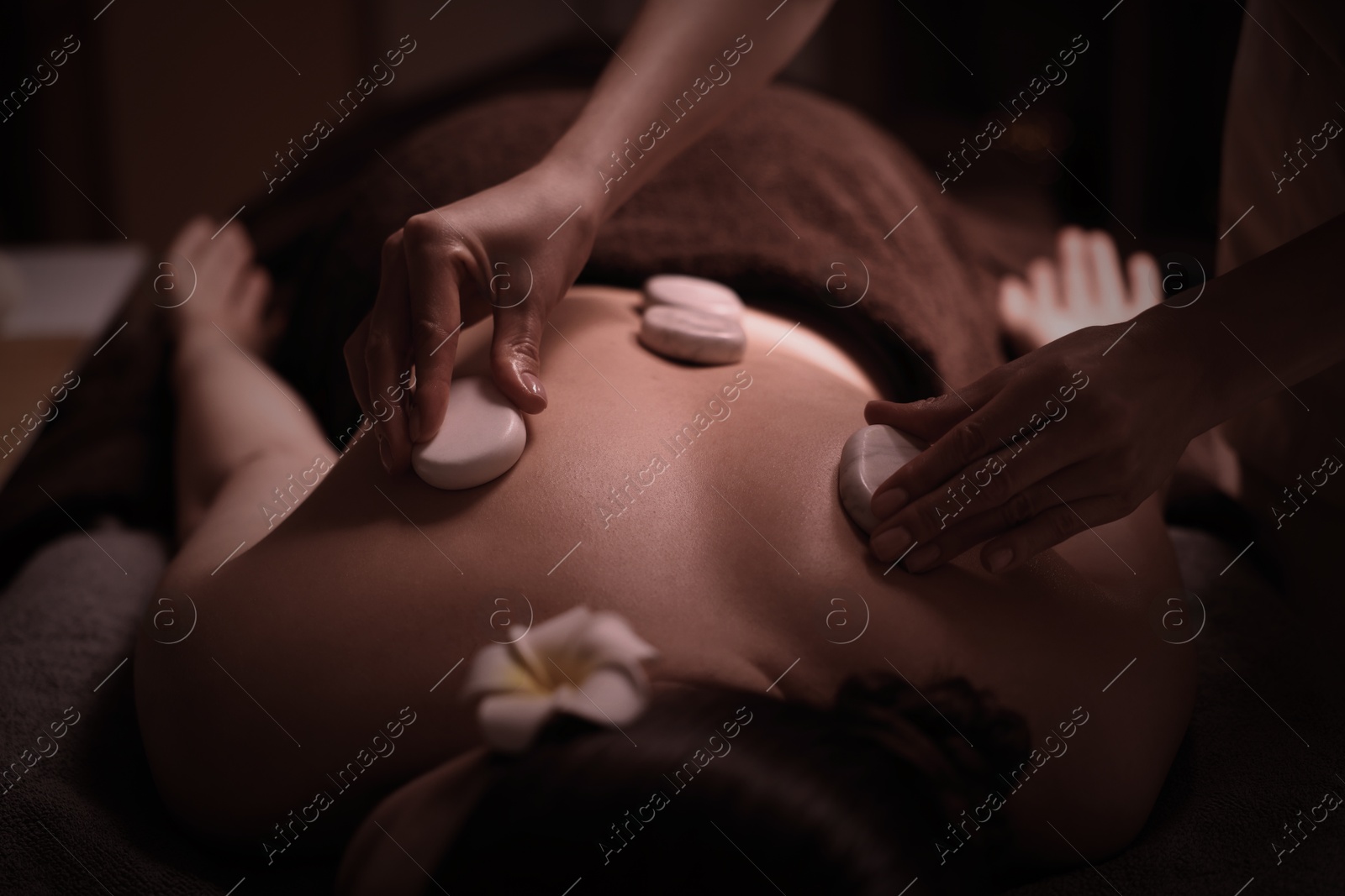 Image of Beautiful young woman lying on table during hot stone massage in salon, closeup