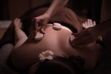 Beautiful young woman lying on table during hot stone massage in salon, closeup