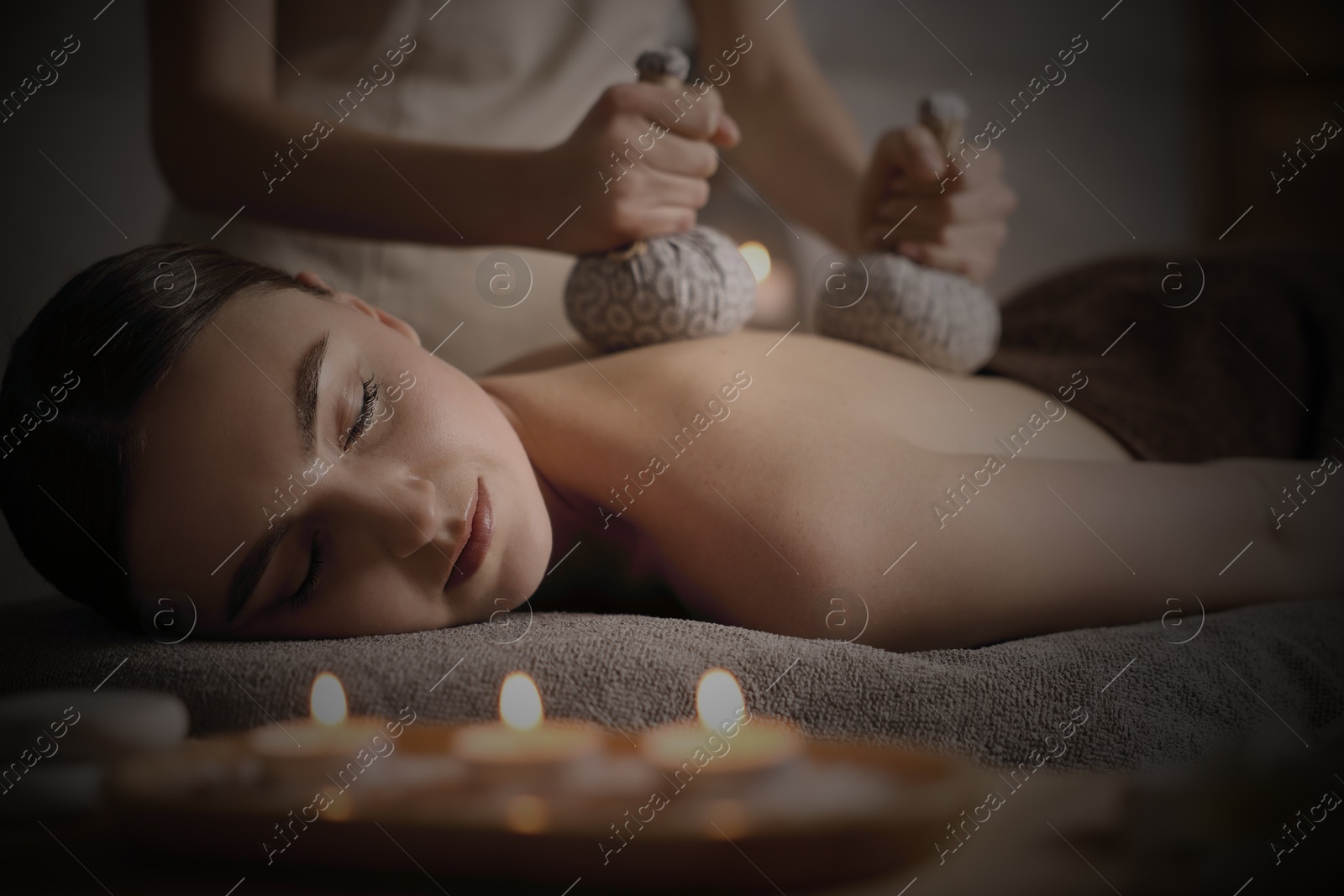 Image of Beautiful young woman lying on table during herbal bag massage in salon