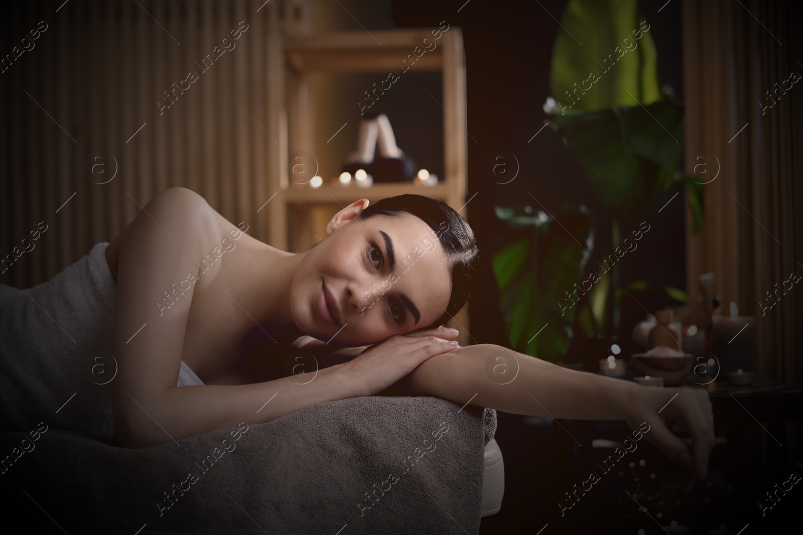 Image of Beautiful young woman lying on massage table in salon, space for text