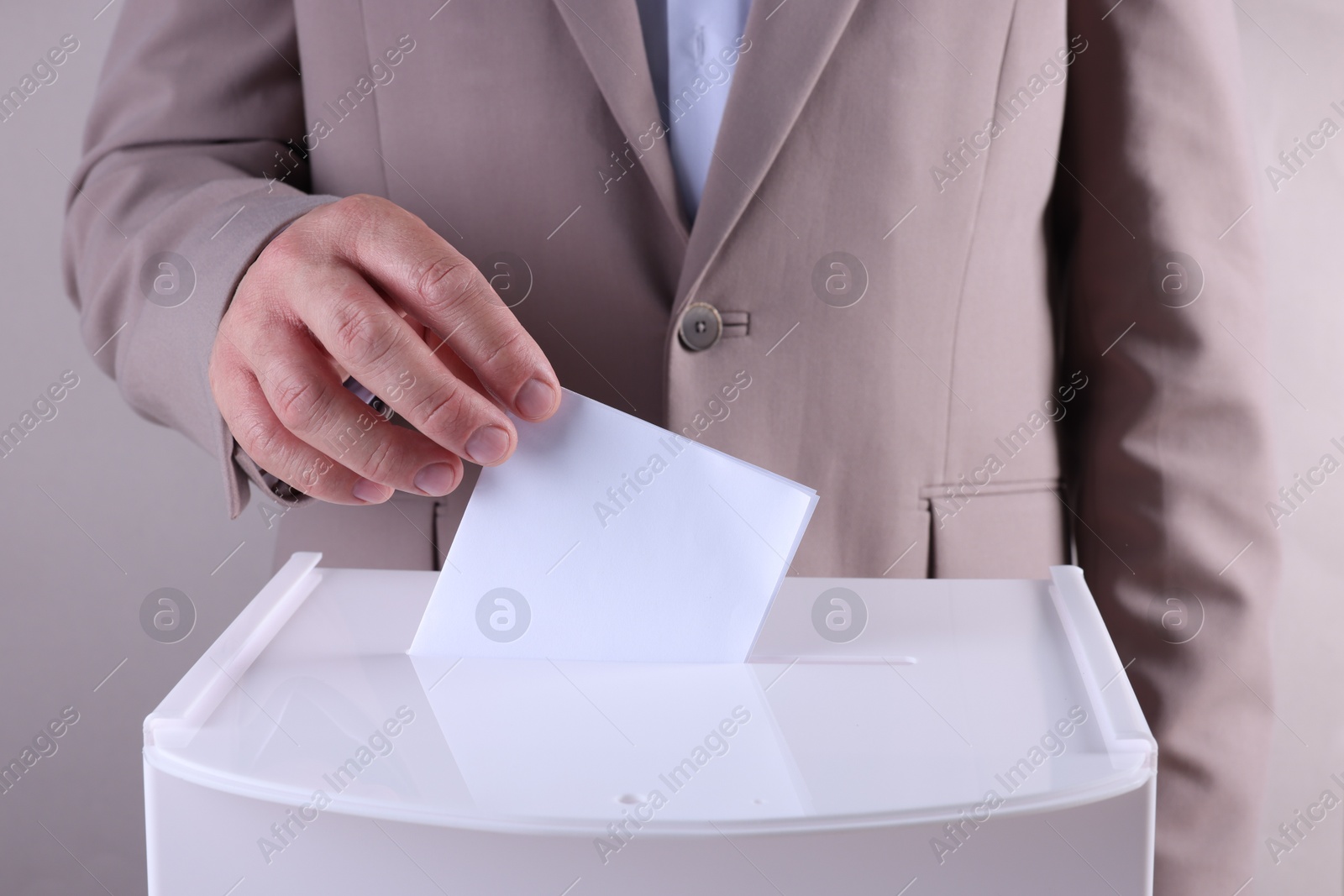 Photo of Man putting his vote into ballot box against light grey background, closeup